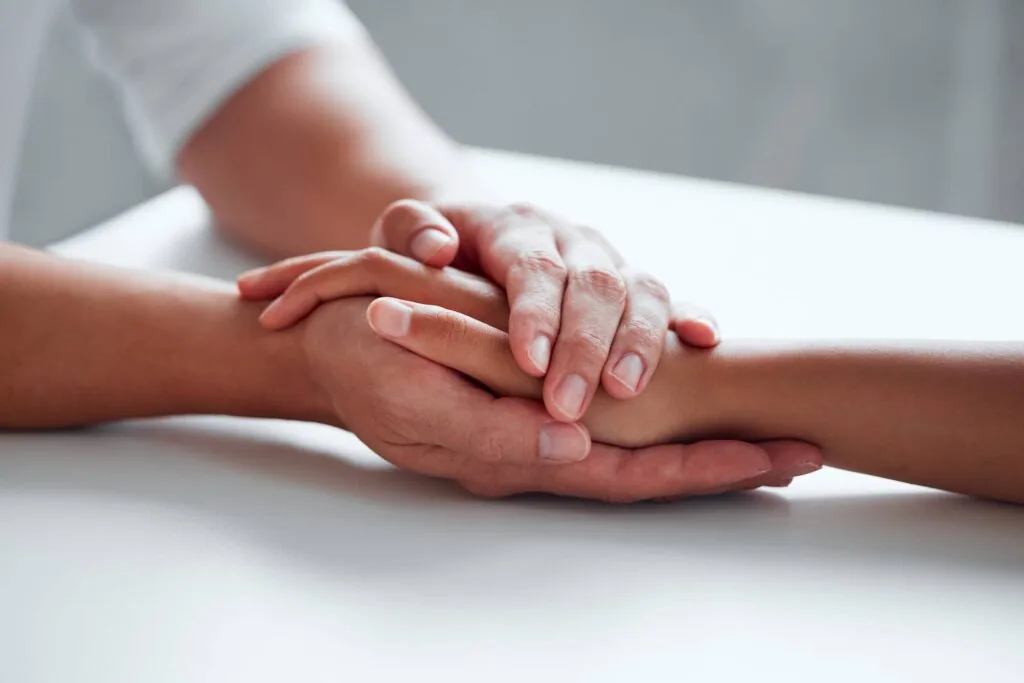 Multiple hands stacked together on a white table surface in a gesture of unity and support