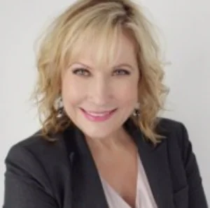 Professional headshot of a woman with blonde wavy hair wearing a black blazer and pink lipstick