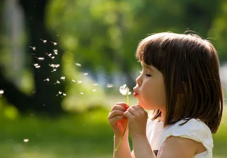 Young girl with brown hair blowing dandelion seeds outdoors in sunlight