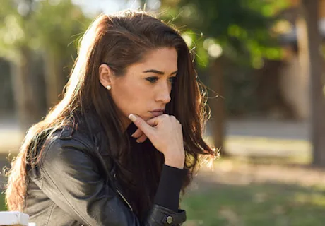 Woman with long dark hair in contemplative pose, resting chin on hand outdoors